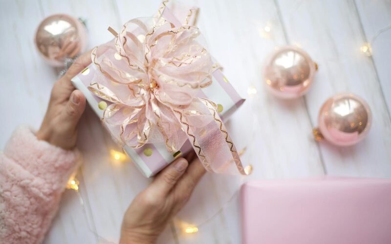 Woman holding wrapped Christmas gift with pink ornaments