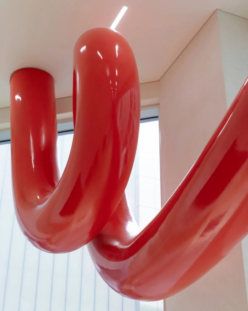 Glossy red tubular sculpture suspended in a modern interior
