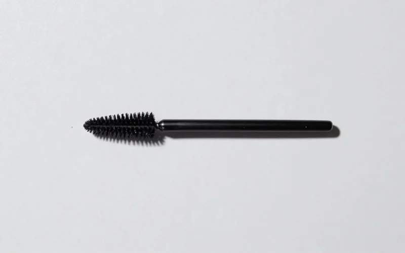 Black mascara wand with bristles on a white background